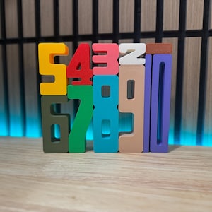 May include: A set of colourful wooden number blocks, arranged in a vertical stack. The numbers are 5, 4, 3, 2, 6, 7, 8, 9, 0, and 1. The blocks are painted in various colours, including yellow, red, pink, white, green, blue, brown, and purple.