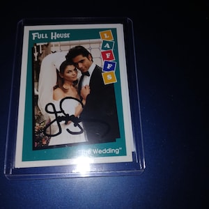 Op de afbeelding: Een verzamelkaart met een kleurenfoto van een stel uit de tv-serie "Full House" in trouwkleding. De kaart heeft de tekst "Full House" en "The Wedding", met een handtekening. De kaart zit in een beschermhoes.