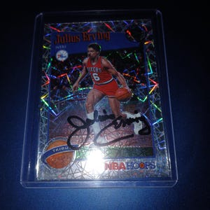 May include: A basketball trading card featuring Julius Erving in a red Philadelphia 76ers uniform, dribbling a basketball. The card has a holographic background and includes the player's signature. The NBA Hoops logo is visible.