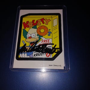 Dan Castellaneta autografió la tarjeta de Krusty el Payaso con coa