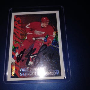 May include: A hockey trading card featuring a player in a red uniform with the number 9. The card has the text "PREMIER STARS" and "FIRST TEAM SERGEI FEDOROV". The card is encased in a protective plastic sleeve.
