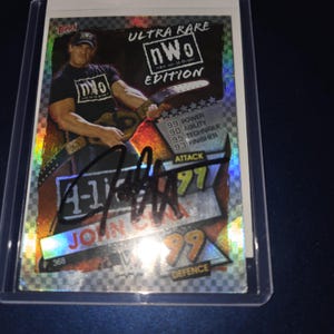 Op de afbeelding: Een John Cena Ultra Rare NWO Edition ruilkaart. De kaart toont een foto van John Cena, met de tekst "ULTRA RARE nWo EDITION". De kaart heeft een handtekening en statistieken voor Power, Agility, Technique en Finisher.