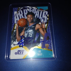 May include: A basketball trading card featuring Ace Bailey of the Utah Jazz. The card has a gold and teal design with the words "Finest Arrivals" at the top. Bailey is holding a basketball and the card is signed.