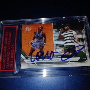 May include: A Topps Now trading card featuring Coco Gauff and Carlos Alcaraz. The card shows action shots of the tennis players on a clay court. The card is encased in a protective holder with a red label that reads "COCO GAUFF, CARLOS ALCARAZ TOPPS NOW CERT #902471."