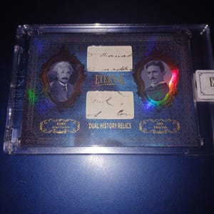 Könnte beinhalten: Eine Sammelkarte mit Porträts von Albert Einstein und Nikola Tesla, mit ihren Unterschriften und dem Text "DUAL HISTORY RELICS". Die Karte ist in einem transparenten Schutzhalter eingeschlossen, mit blauem Hintergrund und goldenen Akzenten.