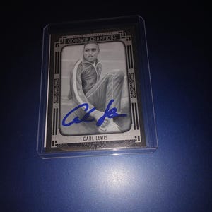 Könnte beinhalten: Eine Schwarzweiß-Sammelkarte mit Carl Lewis, einem Leichtathleten. Die Karte hat einen silbernen Rand und ein schwarzes und goldenes Design. Die Karte stammt aus der Serie Goodwin Champions.