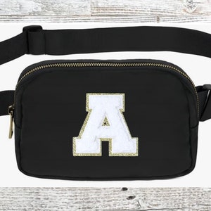 May include: Black fanny pack with a gold zipper and a white felt letter "A" with gold glitter trim.