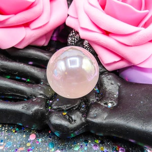 A black skeletal hand holding a pink angel aura rose quartz sphere.