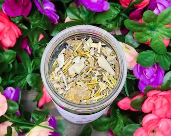 May include: A glass jar filled with a blend of dried herbs and flowers, surrounded by pink and purple artificial flowers.