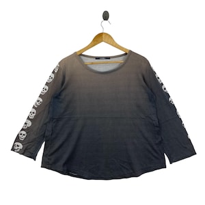 Puede incluir: Una camiseta de manga larga con un efecto de degradado de gris oscuro a negro. Las mangas est&aacute;n adornadas con un patr&oacute;n repetitivo de calaveras blancas. La camiseta tiene un cuello redondo y una etiqueta en el interior que dice LIMI.