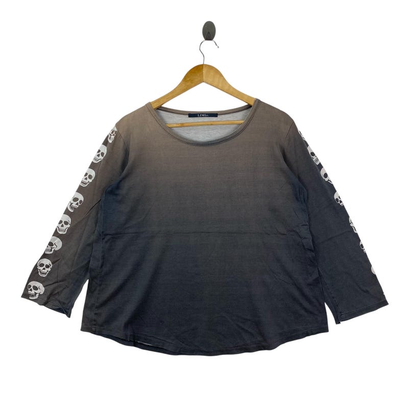 Puede incluir: Una camiseta de manga larga con un efecto de degradado de gris oscuro a negro. Las mangas est&aacute;n adornadas con un patr&oacute;n repetitivo de calaveras blancas. La camiseta tiene un cuello redondo y una etiqueta en el interior que dice LIMI.