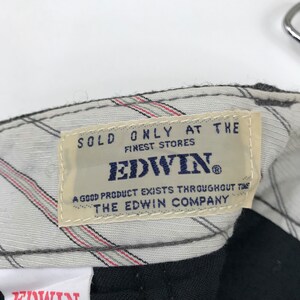 K&ouml;nnte beinhalten: Nahaufnahme eines Kleidungsetiketts mit dem Markennamen "EDWIN" in Marineblau. Das Etikett ist beige mit marineblauem Text, der "SOLD ONLY AT THE FINEST STORES" und "A GOOD PRODUCT EXISTS THROUGHOUT THE THE EDWIN COMPANY" lautet.