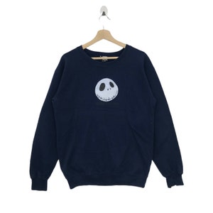 K&ouml;nnte beinhalten: Ein marineblauer Sweatshirt mit einem wei&szlig;en Jack Skellington-Gesichtsmotiv auf der Vorderseite.