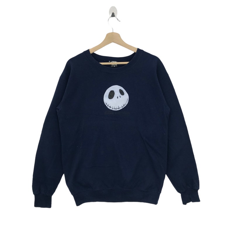 K&ouml;nnte beinhalten: Ein marineblauer Sweatshirt mit einem wei&szlig;en Jack Skellington-Gesichtsmotiv auf der Vorderseite.