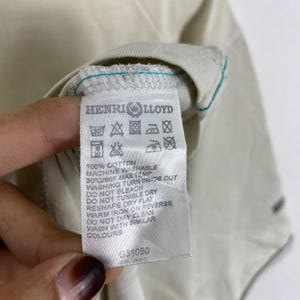 May include: A white garment care label featuring the Henri Lloyd brand name and logo at the top. The label includes various laundry instruction symbols, text specifying 100% cotton, machine wash instructions at 30C/86F, and the code G31050.