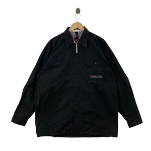 May include: A black long-sleeve zip-up shirt featuring a pointed collar, two chest pockets with button closures, and a rectangular patch on the left chest with the text "ecko unltd". The shirt has a full-length front zipper and buttoned cuffs.