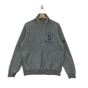 May include: A gray Seattle Mariners fleece pullover with a quarter-zip collar. The team's logo and text are embroidered in navy blue on the chest. The long-sleeved sweatshirt has two front pockets and ribbed cuffs.
