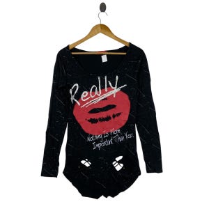 Op de afbeelding: Een zwart shirt met lange mouwen, voorzien van een wit spetterpatroon, een grote rode afbeelding van lippen en de tekst "Really" in zilverkleurig schrift erboven. Onder de lippen staat de tekst "Nothing Is More Important Than You" in het wit.
