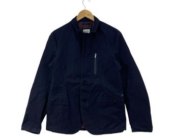 May include: A dark navy blue blazer featuring a structured collar, a front button closure, and a vertical zippered chest pocket. The interior lining is a deep maroon color, and an Armani brand label is visible at the inner neckline of the garment.