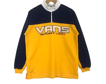 Puede incluir: Una sudadera de vellón amarilla y azul marino con un logotipo blanco "VANS SPORT USA" en la parte delantera.