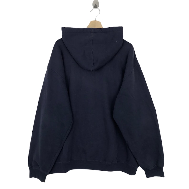 K&ouml;nnte beinhalten: Ein marineblauer Kapuzenpullover mit Kapuze und langen &Auml;rmeln, der an einem Holzb&uuml;gel h&auml;ngt. Die R&uuml;ckansicht des Sweatshirts zeigt das Design der Kapuze und die Gesamtform des Kleidungsst&uuml;cks. Der Kapuzenpullover ist aus einem dicken, weichen Stoff gefertigt.