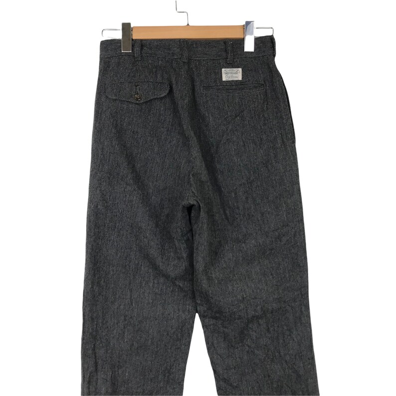 K&ouml;nnte beinhalten: Dunkelgraue Hose mit strukturiertem Stoff, einer gekn&ouml;pften Ges&auml;&szlig;tasche und einem Etikett. Die Hose h&auml;ngt an einem Holzkleiderb&uuml;gel und zeigt die R&uuml;ckansicht des Kleidungsst&uuml;cks.
