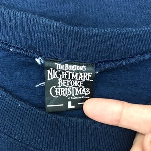 K&ouml;nnte beinhalten: Ein marineblauer Sweatshirt mit einem schwarzen Etikett, auf dem "Tim Burton's Nightmare Before Christmas" und "Touchstone Pictures" steht, sowie ein Gr&ouml;&szlig;enetikett mit "L".