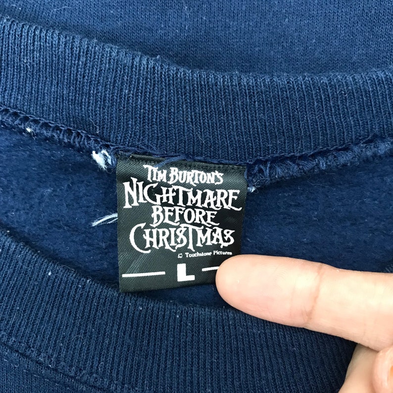K&ouml;nnte beinhalten: Ein marineblauer Sweatshirt mit einem schwarzen Etikett, auf dem "Tim Burton's Nightmare Before Christmas" und "Touchstone Pictures" steht, sowie ein Gr&ouml;&szlig;enetikett mit "L".