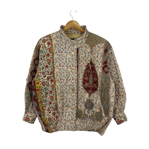 Op de afbeelding: Vintage jas met bloemenprint, een hoge kraag en een knoopsluiting. De jas heeft een mix van patronen, waaronder bloemen- en paisley-ontwerpen in rood, blauw en geel op een crèmekleurige achtergrond. De mouwen zijn lang en gerimpeld bij de manchetten.