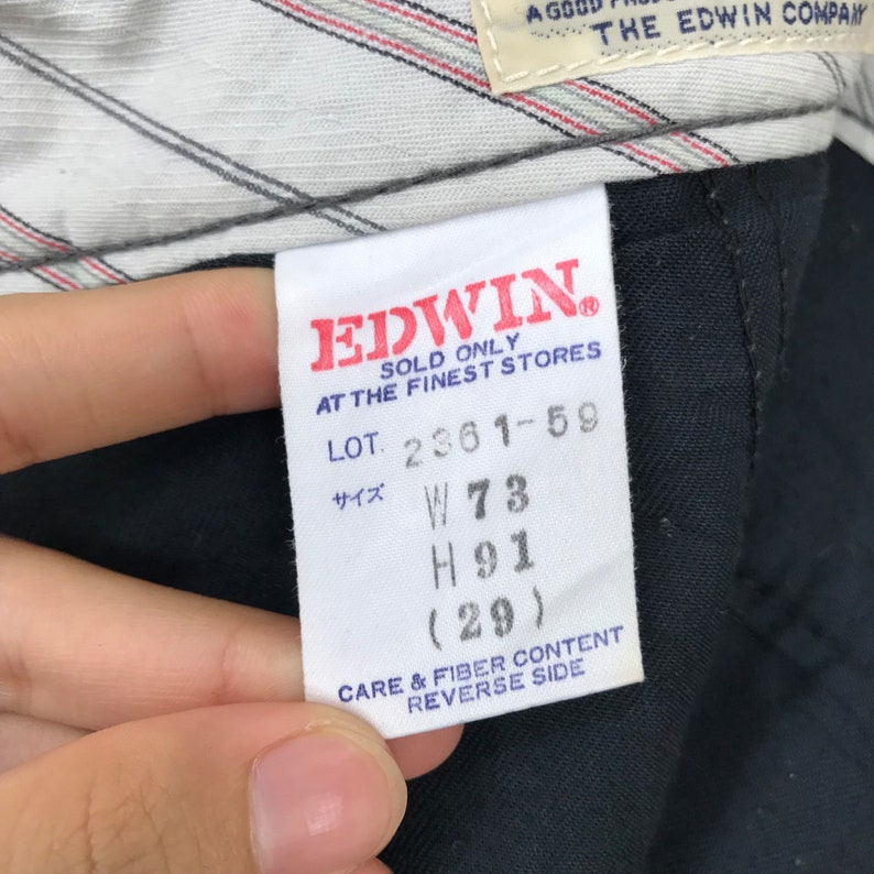 K&ouml;nnte beinhalten: Nahaufnahme eines wei&szlig;en Etiketts mit rotem Text, der "EDWIN" und "SOLD ONLY AT THE FINEST STORES" lautet. Das Etikett zeigt auch "LOT. 2361-59", "W73", "H91 (29)" und "CARE & FIBER CONTENT REVERSE SIDE".
