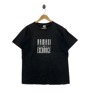 May include: Black t-shirt with the white text "ARMANI EXCHANGE" in a vertical stacked layout. The shirt is hanging on a wooden hanger. The t-shirt has short sleeves and a crew neck.
