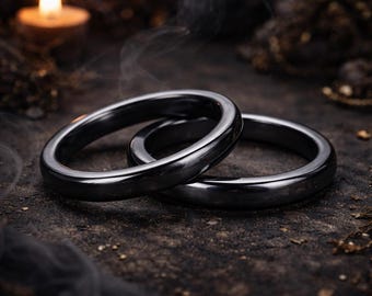 Könnte beinhalten: Zwei glatte, polierte, dunkelgraue Metallringe mit abgerundetem Profil. Die Ringe sind ineinander verschlungen und weisen eine reflektierende Hochglanzoberfläche auf, die das Licht einfängt. Die Bänder sind gleichmäßig dick und kreisförmig.