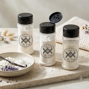 May include: Three clear plastic shaker bottles with black flip-top lids, each containing white powder and featuring a circular label with the text Scents Of The Craft. A small ceramic bowl holds white powder, a vanilla bean, and lavender.