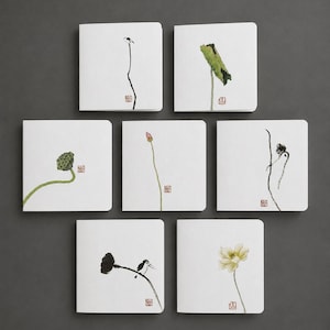 Könnte beinhalten: Ein Set aus sieben quadratischen weißen Grußkarten, die jeweils eine individuelle Tuschezeichnung von Lotusblumen, Samenkapseln oder einem kleinen Vogel zeigen. Jede Karte ist mit einem zarten botanischen Motiv und einem roten Stempel versehen.