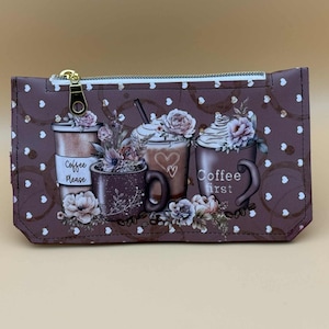 May include: A rectangular brown zippered pouch featuring a repeating white heart pattern and a graphic print of coffee cups, flowers, and coffee rings. The text Coffee Please and Coffee first is printed on the cups with floral accents.