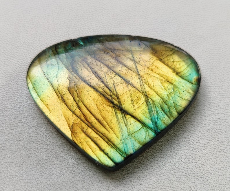 May include: A triangular, iridescent labradorite gemstone with a yellow and green color pattern.