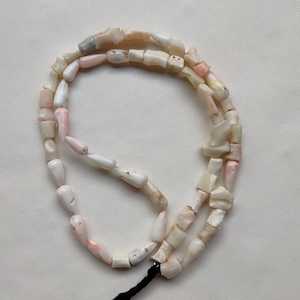 May include: A strand of pink and white shell beads, strung on a black cord. The beads are irregular in shape and size, and some have a pearlescent sheen.
