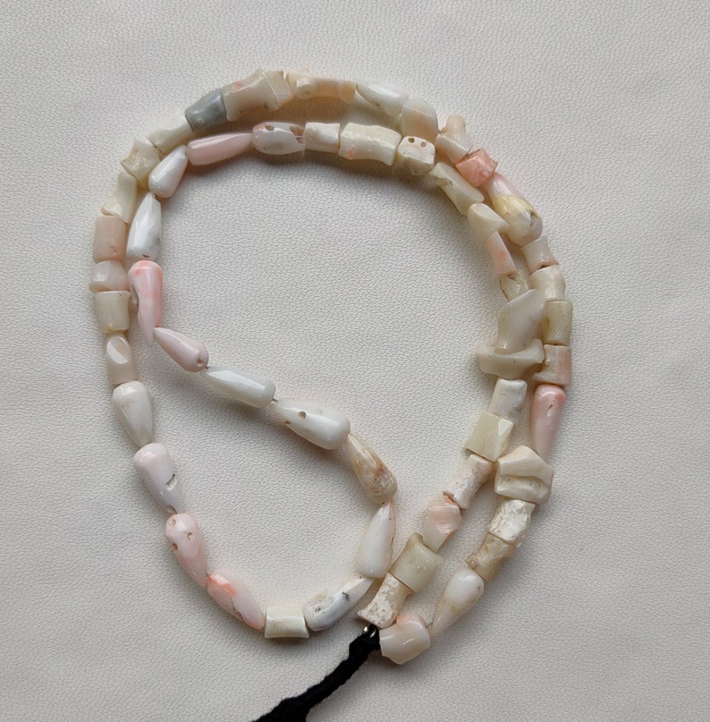 May include: A strand of pink and white shell beads, strung on a black cord. The beads are irregular in shape and size, and some have a pearlescent sheen.