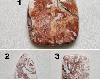 May include: Three polished agate cabochons in various shapes and sizes. The cabochons are a mix of white, brown, and red colors with a swirling pattern.