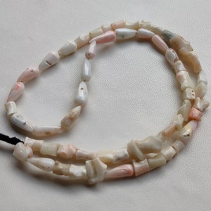 May include: A strand of pink and white shell beads, strung on a black cord. The beads are irregular in shape and size, with some having a more pointed shape.