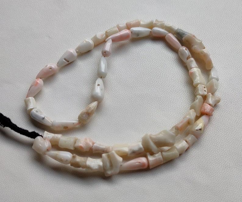 May include: A strand of pink and white shell beads, strung on a black cord. The beads are irregular in shape and size, with some having a more pointed shape.