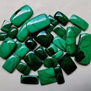 May include: A collection of 20 green malachite cabochons, each with unique patterns and veining. The stones are various shapes and sizes, ranging from small to large.