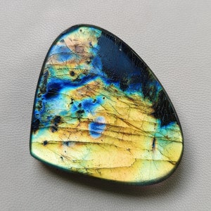 May include: A teardrop-shaped iridescent labradorite gemstone with a blue, green, and gold color pattern.