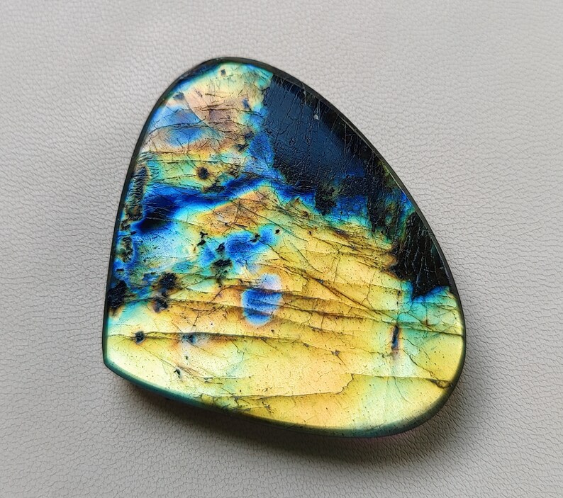 May include: A teardrop-shaped iridescent labradorite gemstone with a blue, green, and gold color pattern.