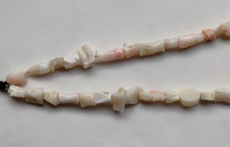 May include: A strand of pink and white coral beads. The beads are irregular in shape and size, and some have a natural, rough texture.