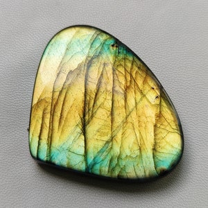 May include: A smooth, heart-shaped labradorite gemstone with a yellow and green iridescent sheen. The stone has a natural, irregular shape and a polished finish.