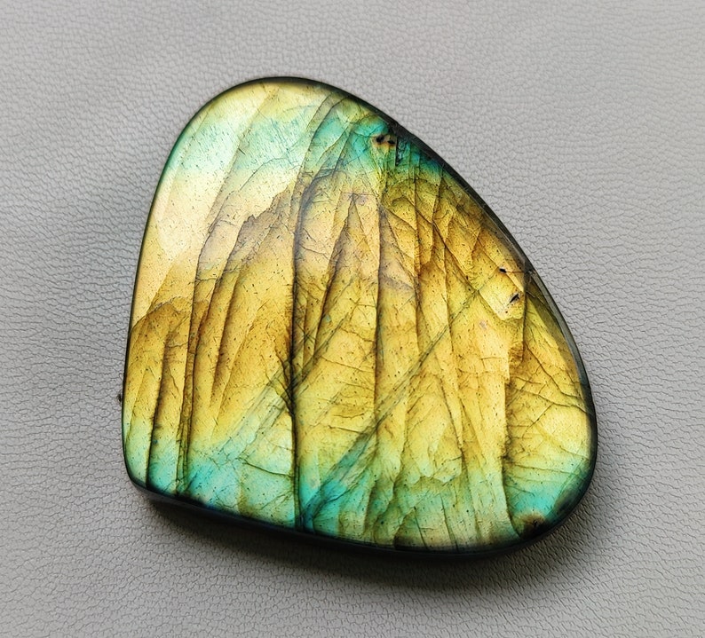 May include: A smooth, heart-shaped labradorite gemstone with a yellow and green iridescent sheen. The stone has a natural, irregular shape and a polished finish.