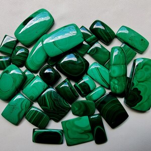 May include: A collection of 20 green malachite cabochons, each with unique patterns and veining. The stones are smooth and polished, with a variety of shapes and sizes.