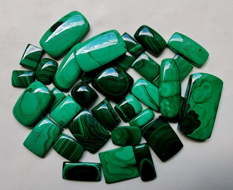 May include: A collection of 20 green malachite cabochons, each with unique patterns and veining. The stones are smooth and polished, with a variety of shapes and sizes.