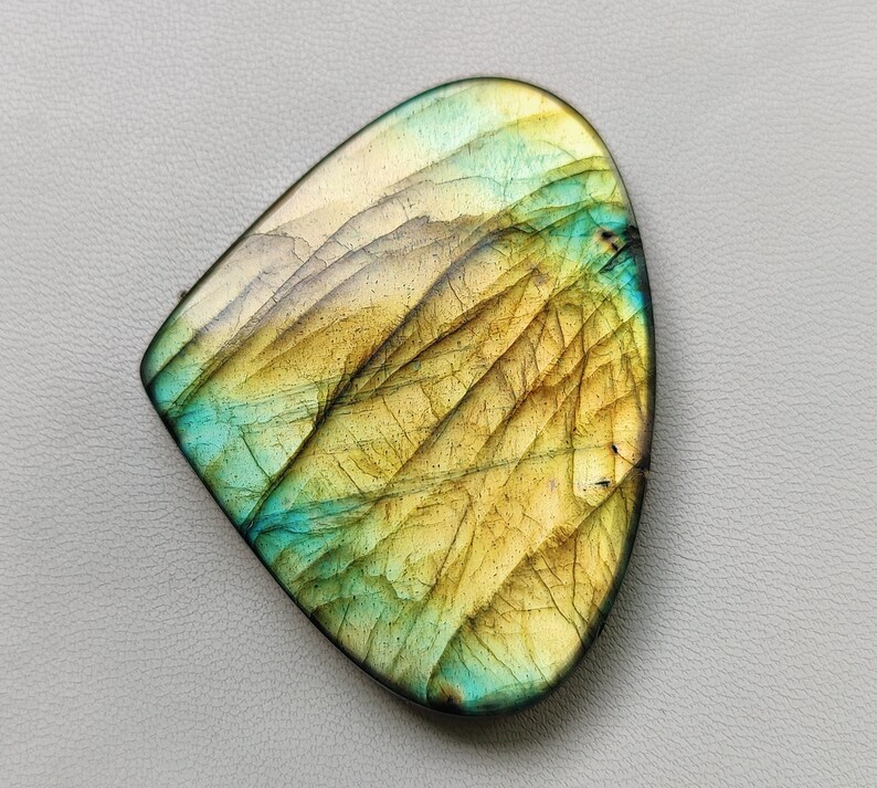 May include: A teardrop-shaped labradorite gemstone with a golden yellow and blue-green iridescent sheen.